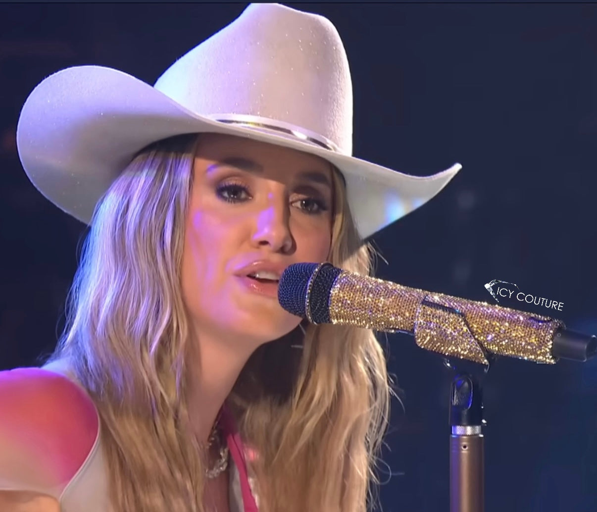 Lainey Wilson singing into her gold bedazzled microphone with small horse shoe crystallized by Icy Couture