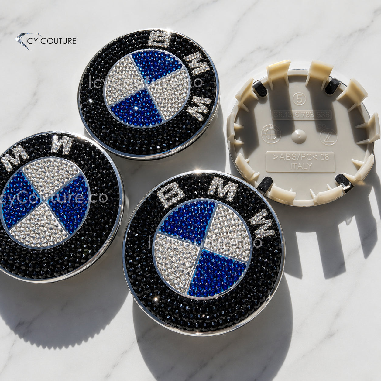 Custom BMW crystal wheel center caps in black, blue, and clear rhinestones with matching replacement cap backing shown by ICY Couture
