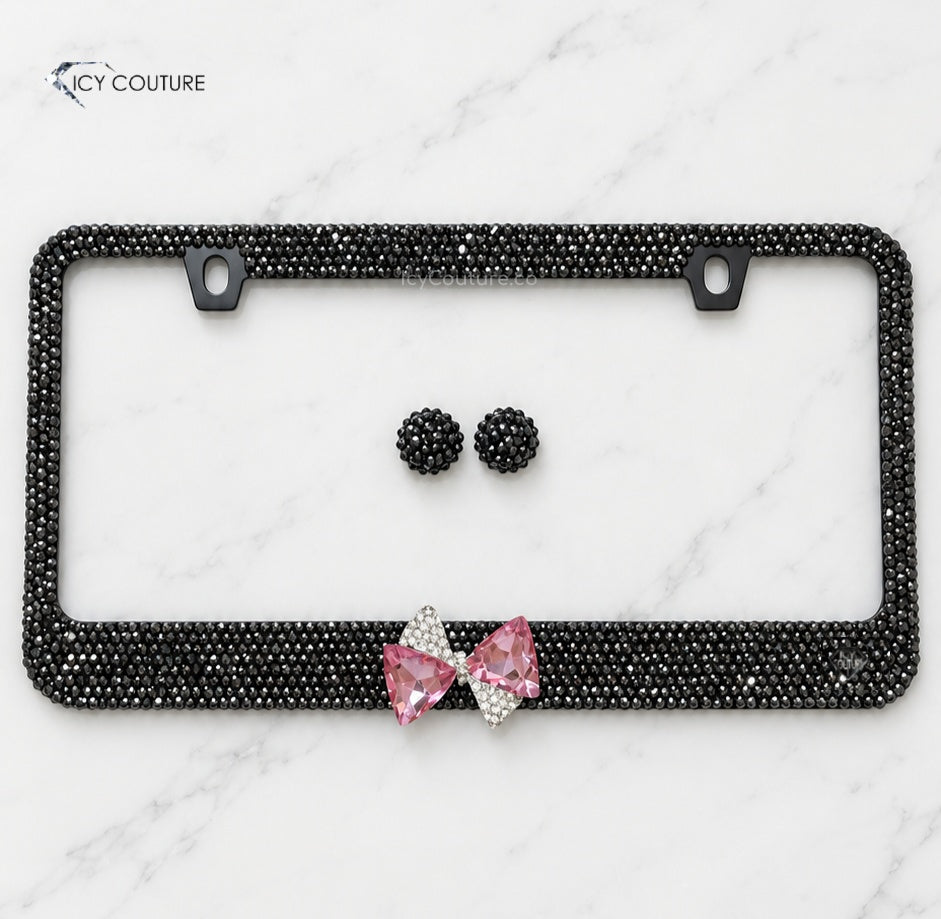 Custom black crystal license plate frame with a pink statement bow and matching rhinestone screw caps by ICY Couture, reflecting natural gunmetal tones of Jet Hematite Swarovski Crystals for luxury car makeover.